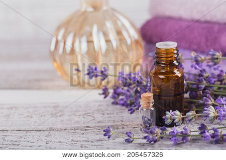 Bottle of essential oil and fresh lavender flowers on a white wooden background. Aromatherapy spa and wellness concept