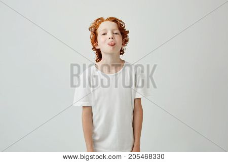 Close up portrait of beautiful ginger kid in white t-shirt showing tongue in camera posing for family photo. Lifestyle concept