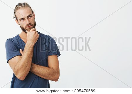 Close up portrait of beautiful bearded man with stylish hairstyle and clothes looking aside and thinking about rooms design