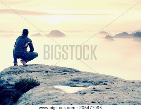 Man stands alone on the peak of rock. Hiker watching to autumn Sun at horizon . Beautiful moment the miracle of nature. Colorful mist in valley. Man hike. Person silhouette stand