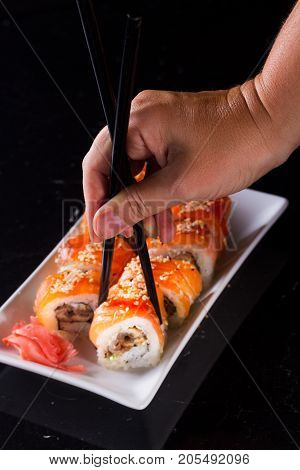 Japanese sushi rolls dish with hand holding one pice in chopsticks on black