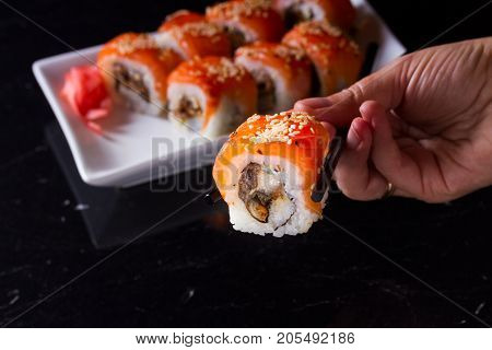 Japanese sushi rolls dish with hand holding one pice in chopsticks, low key