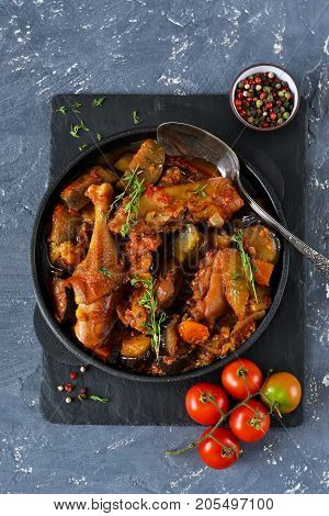 Chicken stewed with vegetables and tomato on a stone board in a frying pan.