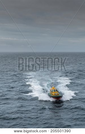 Tasman Sea Australia - March 21 2017: Focus on yellow Pilot boat approaching creating white water trail in dark sea water under rainy dark gray sky.
