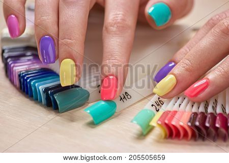 Manicured fingers touching nails samples. Female fingers with bright summer manicure and nails samples. Variety of nails colors in beauty art salon.