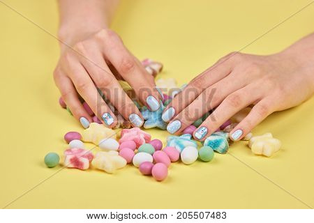 Colorful candies and woman hands. Female hands with beautiful manicure and multicolored candies on yellow background.