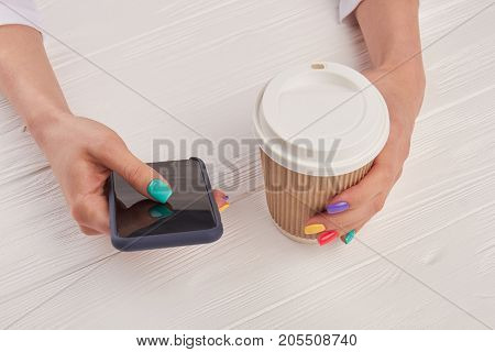 Female manicured hands with smartphone. Woman hand with colorful nails holding touch screen phone and cardboard coffee cup.