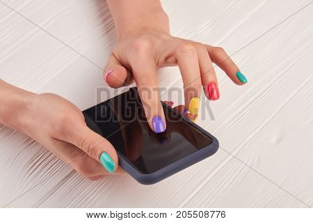 Female manicured hands with smartphone. Girl using a touch screen of smartphone on the wooden table.