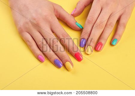 Female well-groomed hands with manicure. Young girl hands polished with different colors nail on yellow wooden background.