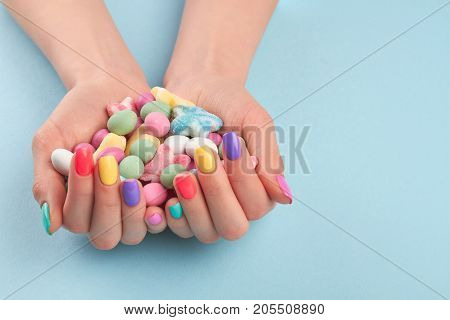 Female hands with colorful candies. Woman hands with stylish colorful nails holding multicolor candies isolated on light blue background.