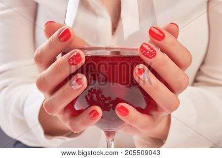 Woman hands holding large glass of wine. Young woman hands with beautiful red manicure holding glass with red wine. Valentines day nail art design.