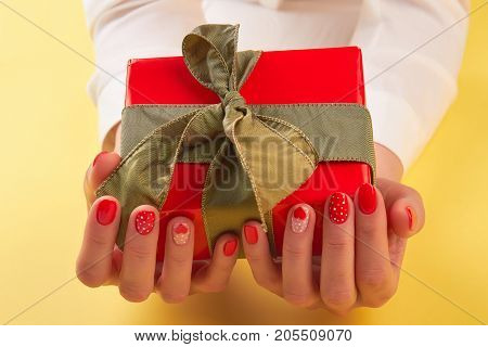 Beautiful gift box in female hands. Woman hands with red manicure holding red box with gift. Holiday and celebration concept.