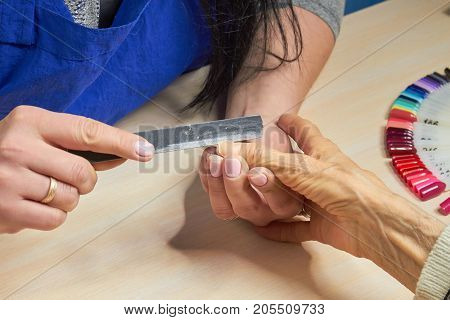 Beautician filing nails to client. Woman hands in nail salon receiving manicure. Old woman is getting manicure in a beauty salon.