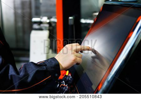 The operator adjusts modern CNC lathe machine using the touch screen. Selective focus.