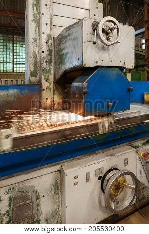 Work of an industrial surface grinding machine. Grinding of a flat metal part. Sparks fly out from under the grinding wheel. Grinding with a coolant.