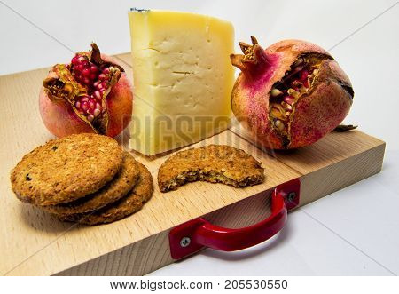 wood chopping board with assortment of cheeses cookies and pomegranate fruit. for food concept