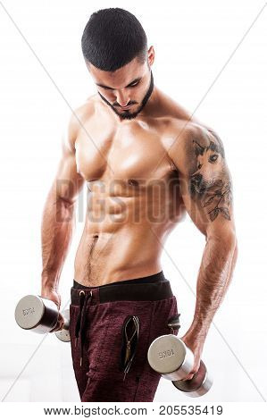 Muscular sexy fitness model posing shirtless over white background. Studio shot of Athletic young man with tattooed torso standing with dumbbells. Strength and motivation concept.