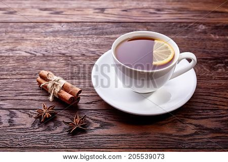 White porcelain cup of tea with cinnamon sticks, lemon, mint leaves and tea strainer on wooden rustic table.