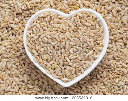 Brown rice in heart-shaped bowl on rice background. Copy space. Top view or flat lay.