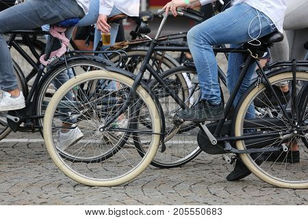 boy with blue jeans pedal on a black bicycle with many other bikes on the street