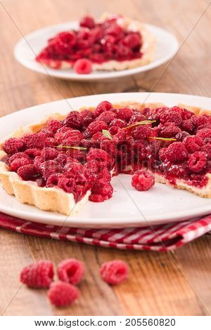 Raspberry tart with fresh rasperries in white bowl.
