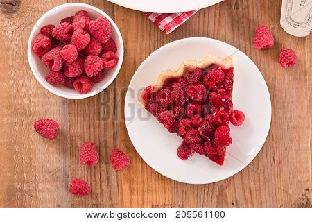 Raspberry tart with fresh rasperries in white bowl.