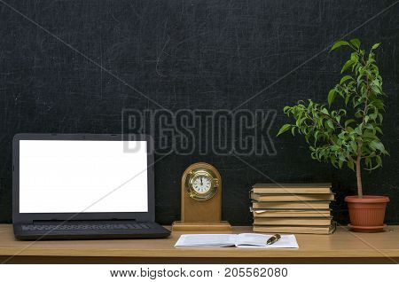 Teacher or student desk table. Education background. Education mockup concept. Laptop with blank screen plant in the pot stacked books copybook and clock watch on blackboard background.