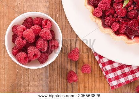 Raspberry tart with fresh rasperries in white bowl.