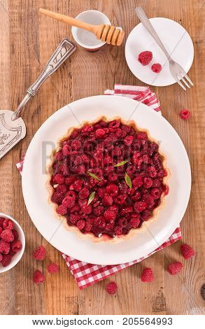 Raspberry tart with fresh rasperries in white bowl.