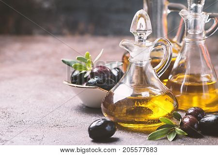 Olive oil in a glass bottle and olive branch on brown stone table
