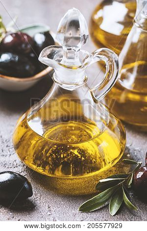 Olive oil in a glass bottle and olive branch on brown stone table