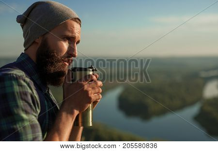 Side view of hipster stylish man having drink from thermomug in nature.