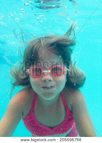 a little girl swimming underwater with goggles on.