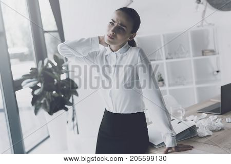 Sick woman sitting at her workplace in the office. Her neck stiffened and she held onto her. The woman got up from her workplace to stretch