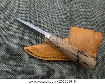 A fixed blade damascus knife and leather sheath displayed on a blurred burlap background. Both items are hand crafted making them a unique set.