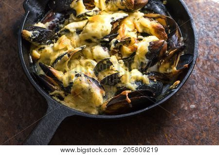 Frying pan with mussels under cheese sauce on a brown background side view horizontal