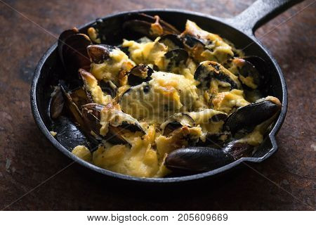 Cooked mussels in a cast-iron frying pan with cheese sauce horizontal