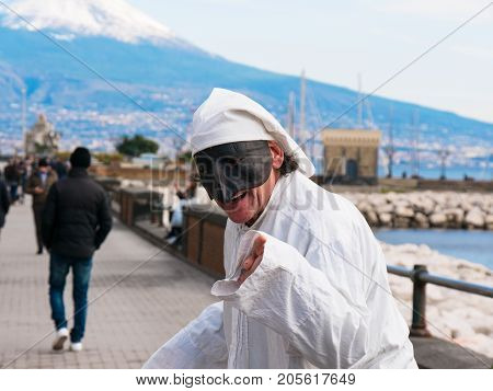 Pulcinella and people, traditional Neapolitan mask gestures with snowy Vesuvius in the background in the Gulf of Naples. Actor recites the part of Pulcinella in the street, among the people who pass, on the promenade of Naples