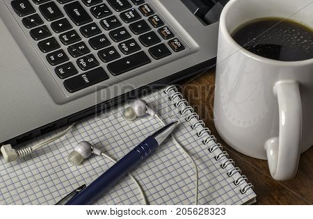 Laptop, headphones, notebook and  cup of coffee on the computer desk