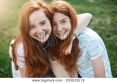 Two identical sisters have so much in common. Hugging, smiling, spending time together outdoor on a sunny day. Twins are what boys dream of.