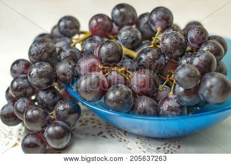 Black grapes on a plate on a white tablecloth.