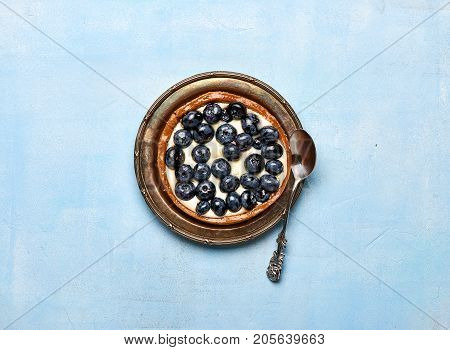 Blueberry tart, pie, tartlet with custard on blue stone background.