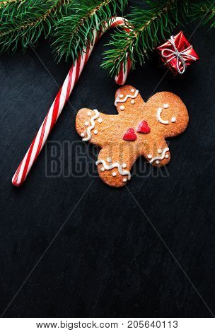 Christmas Decorations with Christmas gift box Gingerbread man cookie fir tree branches and candy stripe red stick on dark background with copyspace. Xmas holiday symbols