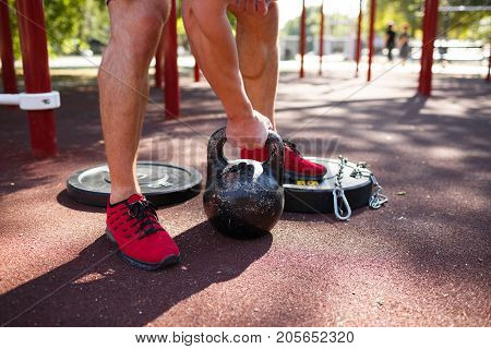 A strong man with sexy body is doing exercises on his feet. A handsome young man lifts weights with his feet in the park.