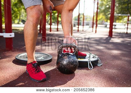 A strong man with sexy body is doing exercises on his feet. A handsome young man lifts weights with his feet in the park.