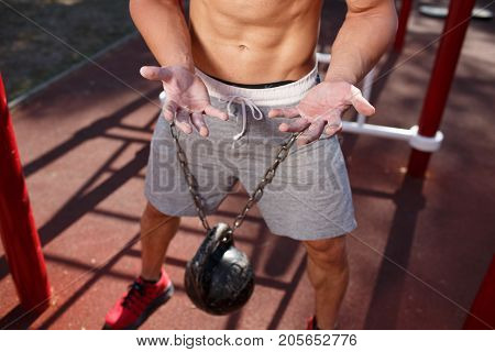 A strong man with sexy body is doing exercises on his feet. A handsome young man lifts weights with his feet in the park.