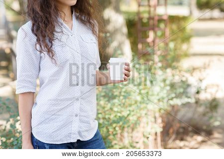 Pretty woman holding in her hands a cup of coffee on the nature. Close-up of drink.