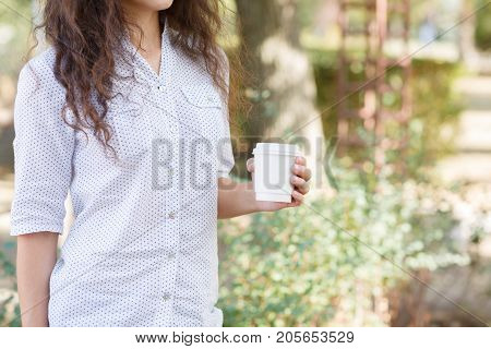 Pretty woman holding in her hands a cup of coffee on the nature. Close-up of drink.