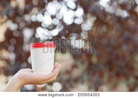 Human holding in the hand a cup of coffee on the nature. Close-up of drink.