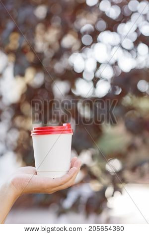Human holding in the hand a cup of coffee on the nature. Close-up of drink.